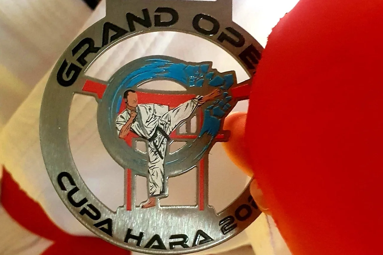 Medalia argintie „Grand Open Cupa Hara”, cu un karateka care lovește din picior, ținută de o mănușă roșie.