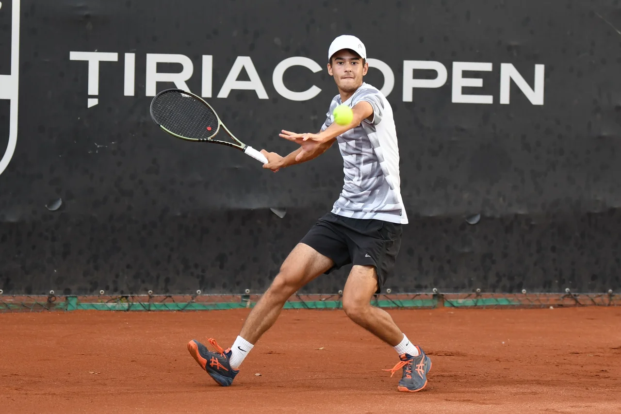 Ștefan Andreescu, cu șapcă albă, lovește din forehand pe zgură, în fața panoului Țiriac Open.