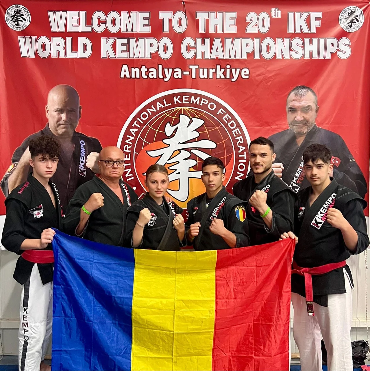 Sportivii de kempo în kimonouri negre țin steagul României sub bannerul „Welcome to the 20th IKF World Kempo Championships, Antalya-Turkiye”.