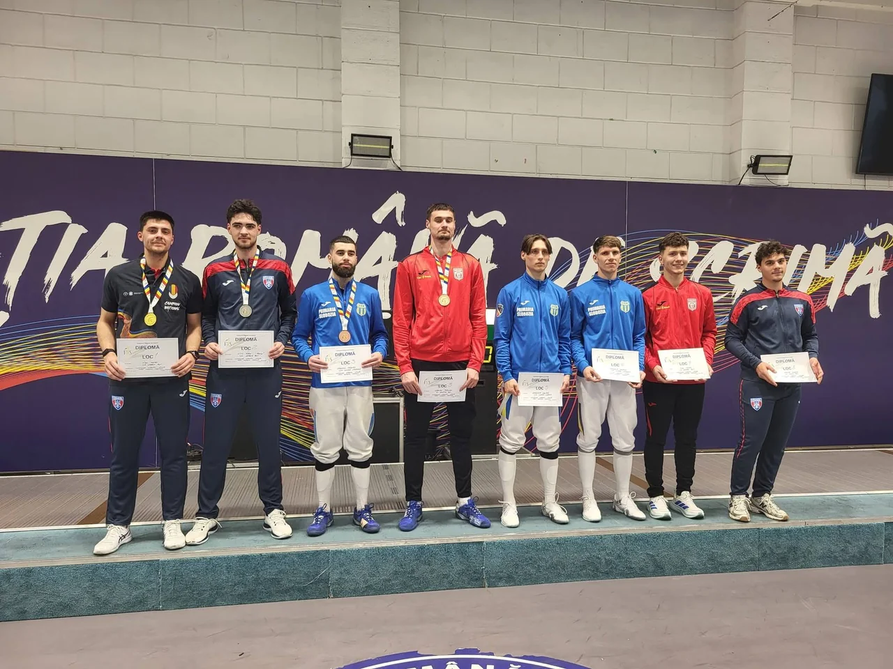 Sabrerii medaliați pe echipe, cu diplomele, pe podiumul Campionatului Național, în fața panoului Federației Române de Scrimă.