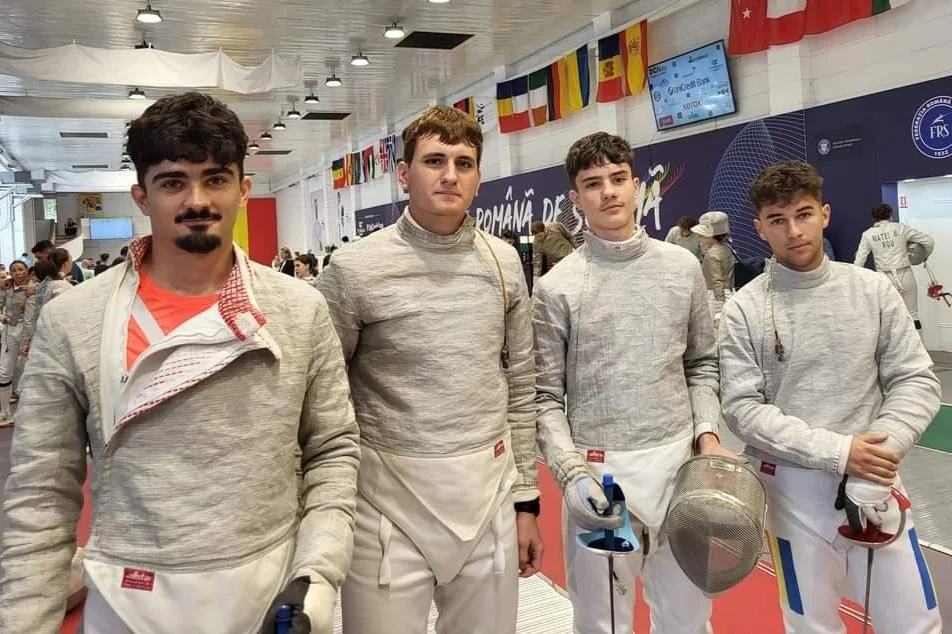Echipa de sabie a clubului, patru sportivi în costume albe de scrimă, în sala de concurs.
