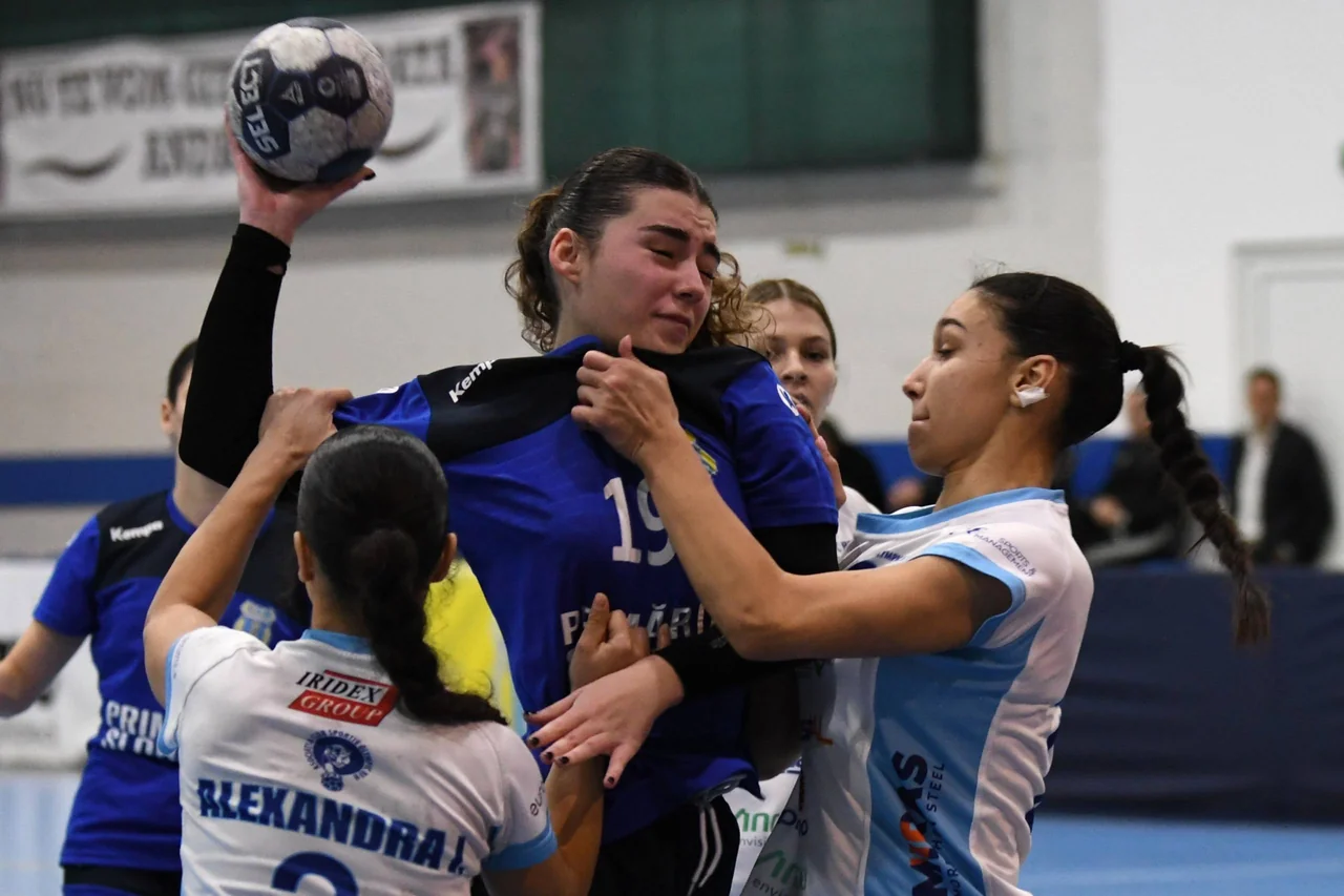 O junioară a CSM Unirea Slobozia, în albastru, ține mingea sus, înconjurată de apărătoare în alb cu albastru.