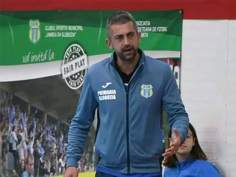 Un antrenor de handbal al clubului vorbește în fața unui banner „Fair Play”, cu o jucătoare așezată lângă el.