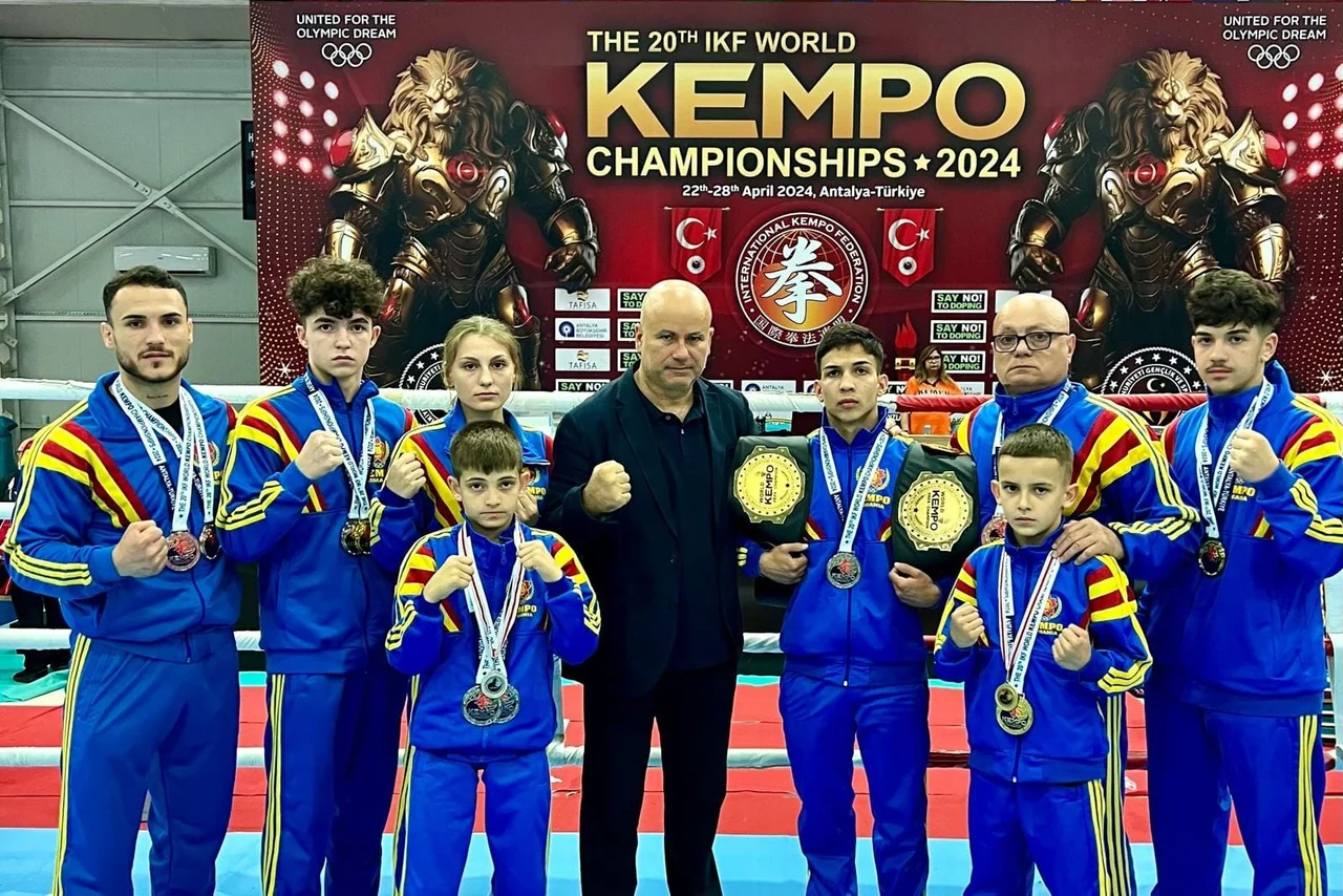 Lotul de kempo, cu medalii și centuri de campion, în fața afișului „The 20th IKF World Kempo Championships 2024, Antalya”.