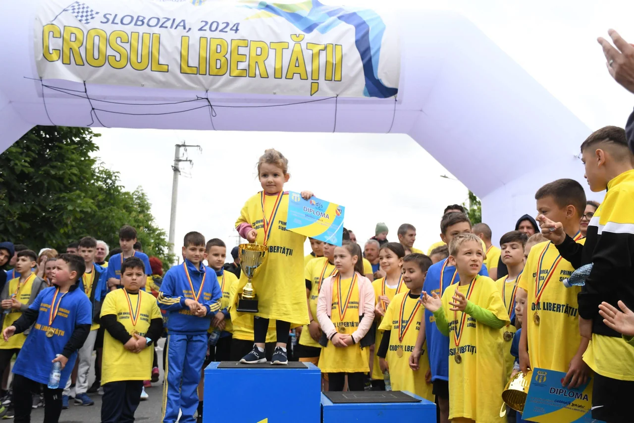 O fetiță pe treapta cea mai înaltă a podiumului, cu medalie și diplomă, la premierea celor mici de la Crosul Libertății.