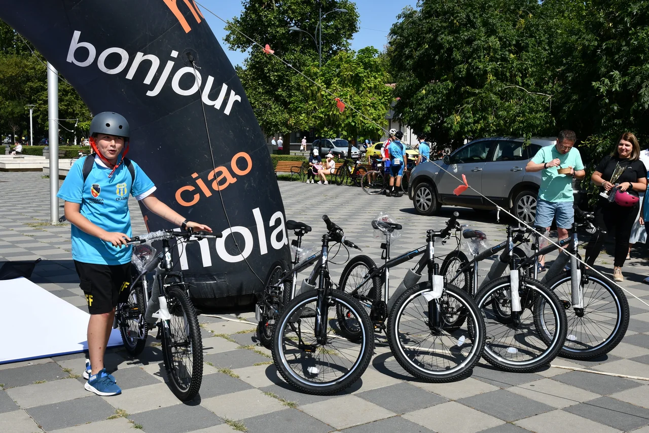 Un copil cu cască și tricou albastru ține una dintre bicicletele oferite la tombola concursului, lângă celelalte biciclete.