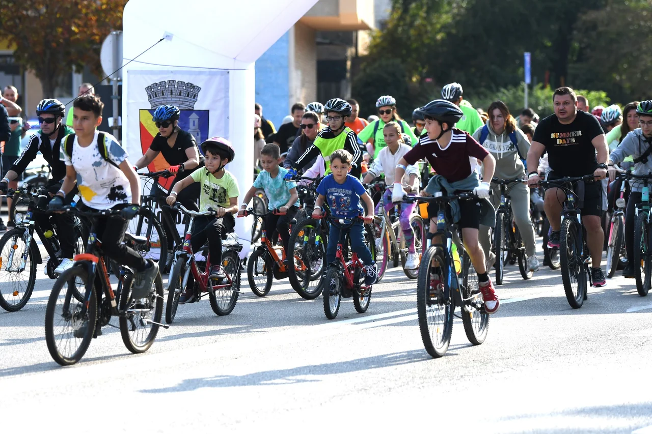 Copii și adulți pe biciclete pornesc de sub arcada de start la o tură de pedalat prin centrul Slobozia.