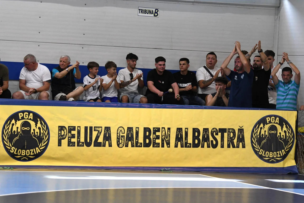 Suporteri, adulți și copii, aplaudă în tribună deasupra bannerului „Peluza Galben Albastră PGA Slobozia”.