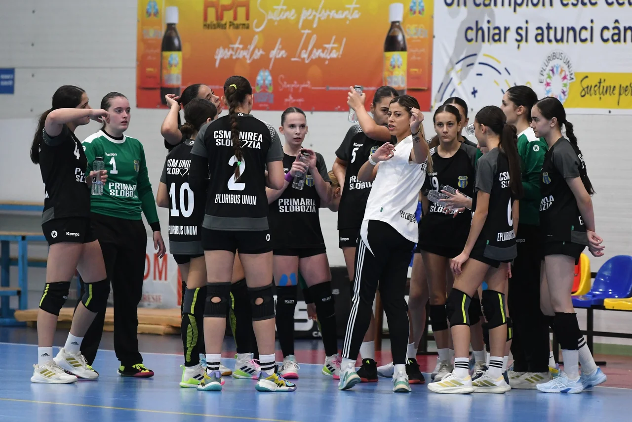 Echipa de Junioare 2, în tricouri negre, și portarul, în verde, în jurul antrenoarei, în Sala Sporturilor din Slobozia.