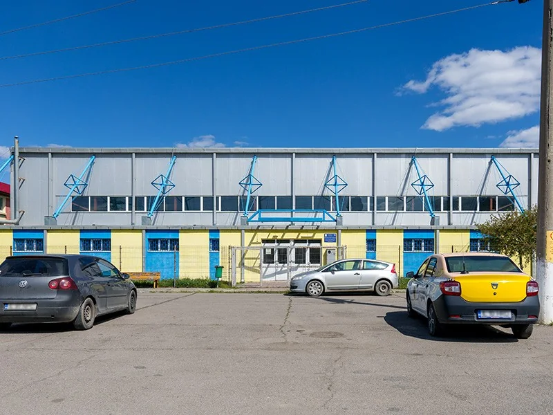 Sala de sport „Al. I. Cuza” văzută din parcare: o hală lungă, cu ferestre sus și uși albastre.