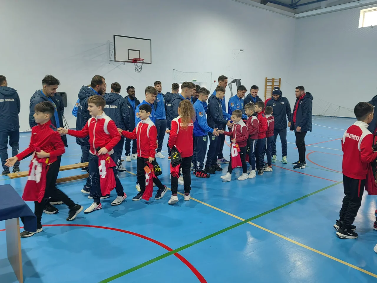 Copiii de la CSM Fetești dau mâna, pe rând, cu fotbaliștii Unirii Slobozia, în sala de sport.