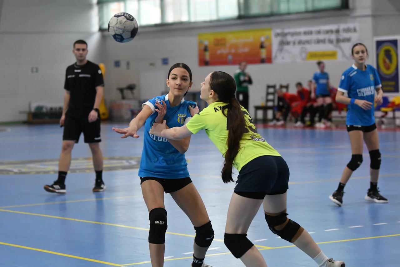 O junioară a CSM Unirea Slobozia, în albastru, pasează pe lângă o adversară în galben; arbitrul urmărește faza.