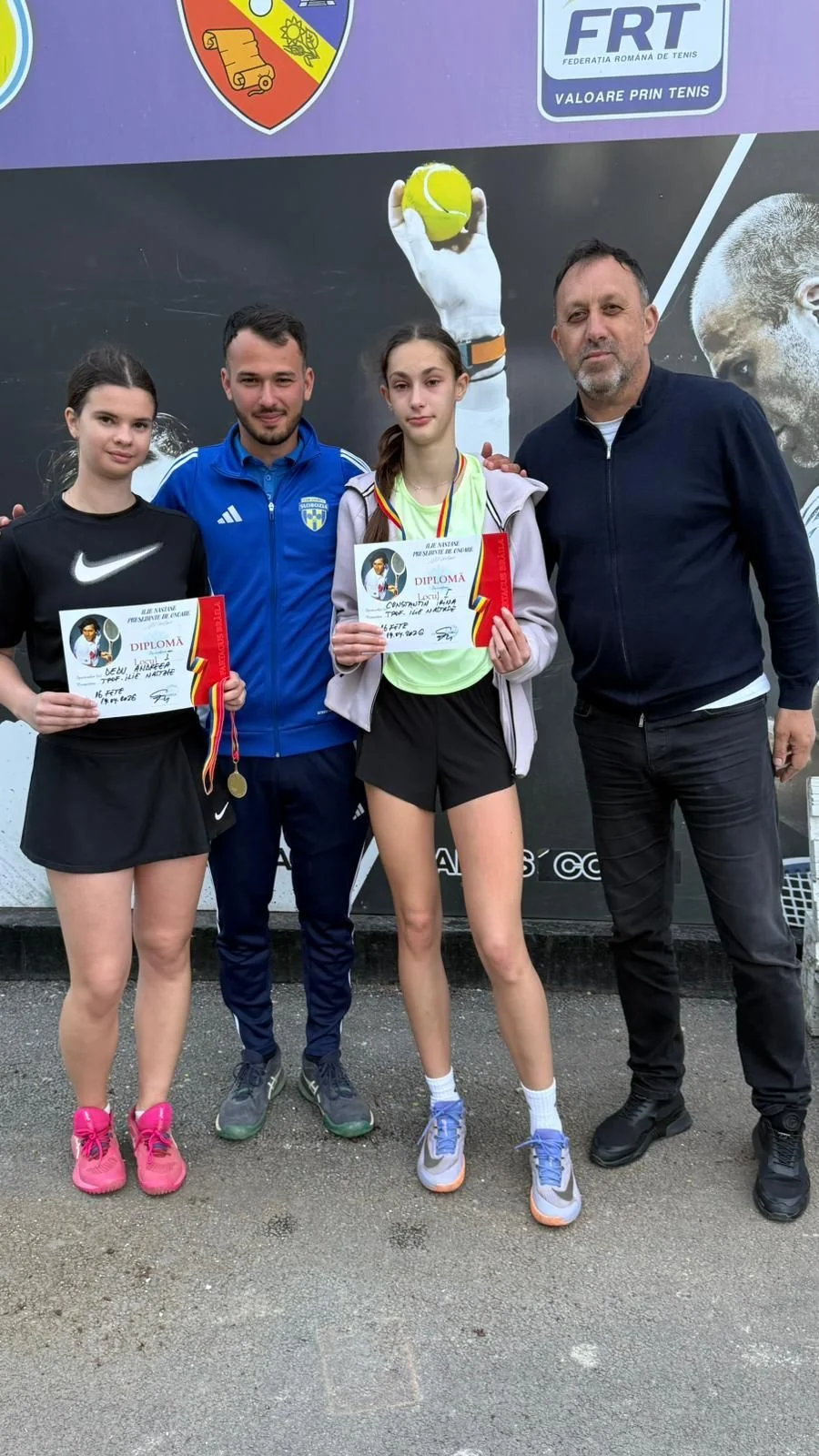 Cele două tenismene ale clubului, Andreea Dedu și Irina Constantin, cu diplomele, alături de doi antrenori, în fața panoului FRT.
