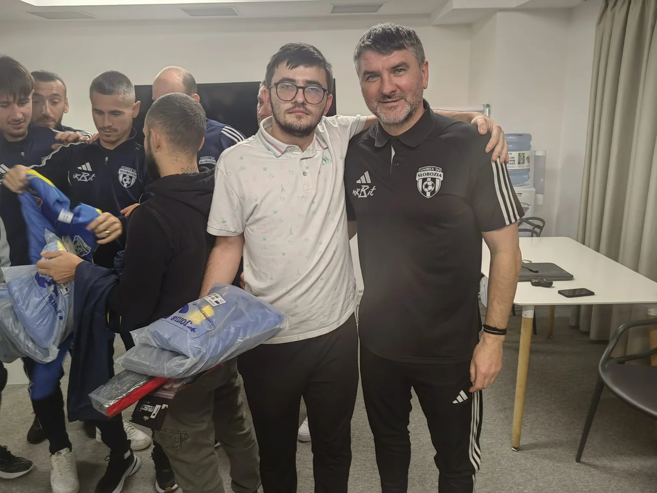 Un membru al conducerii Unirea Slobozia îmbrățișează un suporter, printre jucători și pungi cu echipament donat.