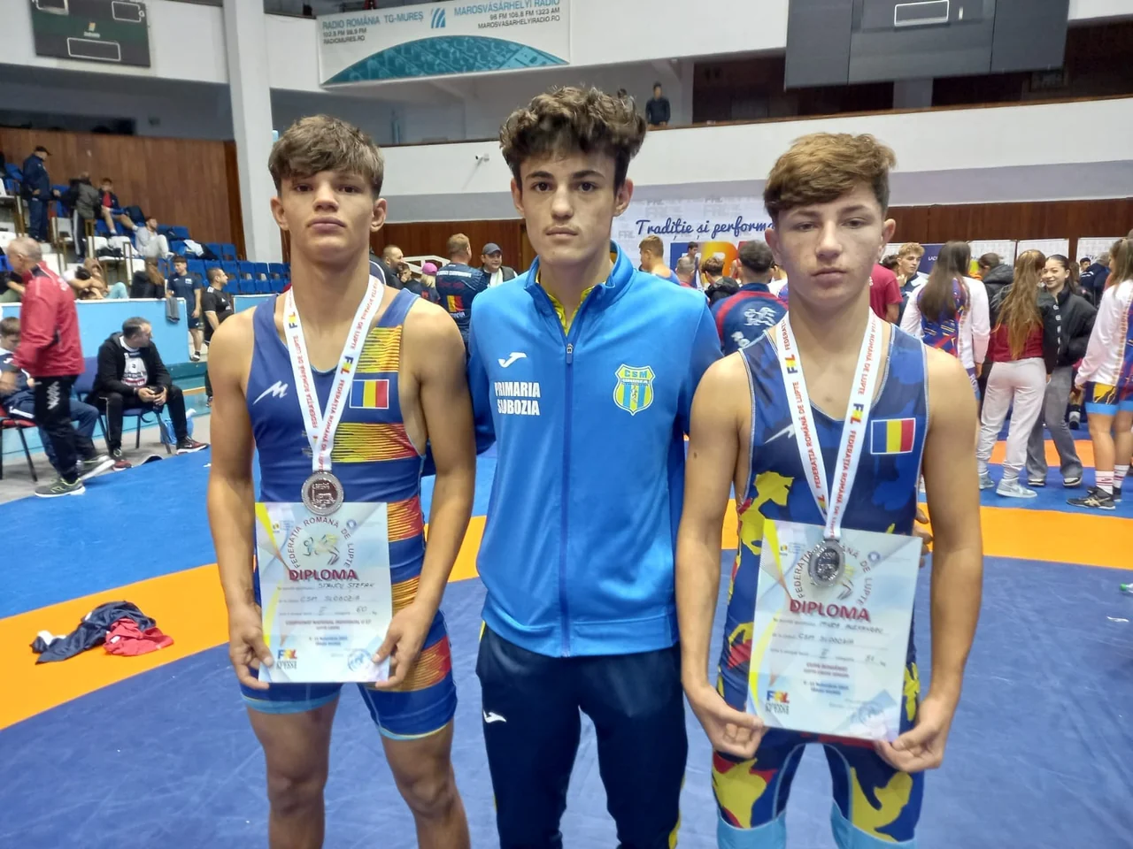 Cei doi luptători medaliați cu argint la Campionatul Național U17, cu diplomele în mâini, alături de un coleg în trening albastru.