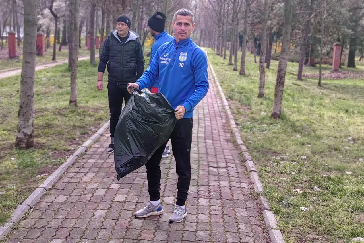 Un fotbalist al Unirii Slobozia duce un sac negru plin cu gunoaie pe aleea din parc, urmat de colegi.